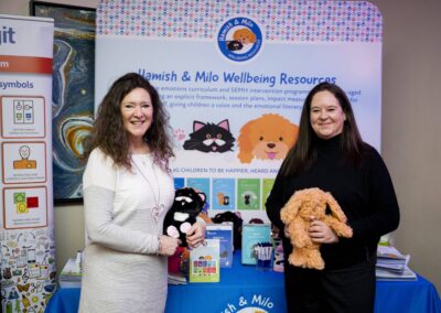 Anne and Clare from Hamish and Milo stand in front of their exhibition space holding their plush dolls.